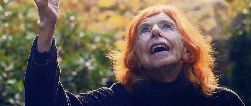 Closeup image of dancer Edith Stephen (95) looking upwards. She is wearing green eyeshadow and has bright orange hair.